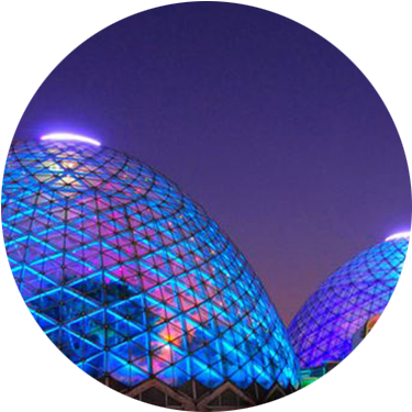Two of the three mitchell park glass domes are lit up in blues, purples, and reds at night.